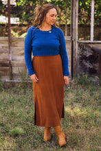 Load image into Gallery viewer, A woman standing outdoors on grass in front of a rustic wooden structure, wearing a bright blue long-sleeve knit sweater and a brown midi skirt with side slits, paired with tan ankle boots.
