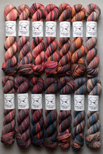 Load image into Gallery viewer, Row of skeins of multicolored yarn with labels on a neutral background
