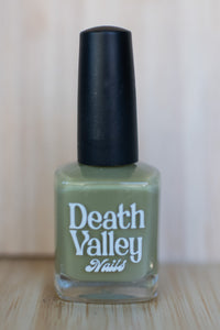 Green nail polish bottle with black cap on a wooden surface