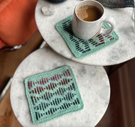 Two knitted coasters on a marble surface with a cup of coffee.
