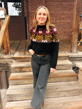 Load image into Gallery viewer, Woman wearing a patterned sweater and jeans standing on wooden steps.