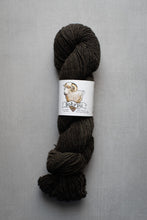 Load image into Gallery viewer, A skein of dark brown yarn with a white paper label featuring a sheep illustration and the brand name set against a neutral gray background.