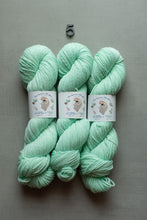 Load image into Gallery viewer, Three skeins of mint green yarn with white paper labels, arranged vertically on a gray background with a small metal size marker above them.