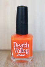 Load image into Gallery viewer, Bottle of orange nail polish with black cap labeled &#39;Death Valley Nails&#39; on a wooden surface.