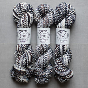 Three skeins of yarn with 'Plump Spincycle Yarns' labels on a gray background