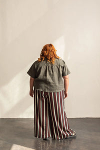 Person wearing a green top and striped pants standing against a plain wall.