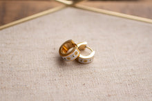 Load image into Gallery viewer, Gold hoop earrings with floral designs on a textured fabric surface