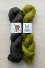 Load image into Gallery viewer, Two skeins of wool yarn on a light beige textured background. The left skein is a dark charcoal gray with a white paper label featuring a bull illustration and the text 'Best Powder'.