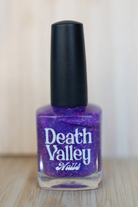 Purple nail polish bottle with black cap on a wooden surface
