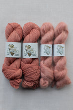 Load image into Gallery viewer, Four skeins of yarn arranged in two rows of two on a light gray fabric background. The left two skeins are a muted dusty rose, and the right two are a dusty peach pink.