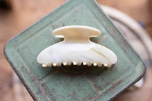 Load image into Gallery viewer, White hair clip on a green metal surface