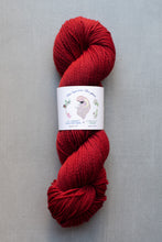 Load image into Gallery viewer, Red skein of yarn with a label on a gray background