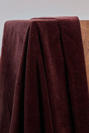 Close-up of a folded burgundy fabric with a textured pattern on a neutral background