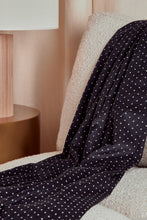 Load image into Gallery viewer, Black polka dot blanket draped over a chair in a cozy room with a lamp and side table.