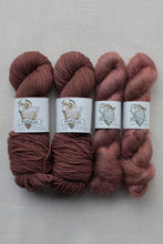 Load image into Gallery viewer, Four skeins of yarn in earthy dusty rose and mauve shades, arranged side by side on a light gray textured background. Each skein has a white paper label with a ram illustration and the brand name 'Pebble Mill'.