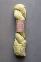 Load image into Gallery viewer, Light yellow skein of yarn with a pink label on a gray background