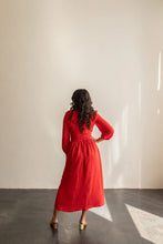 Load image into Gallery viewer, Woman in a red dress standing against a white wall