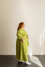 Load image into Gallery viewer, Woman wearing a green dress standing against a plain wall.