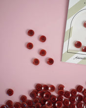 Load image into Gallery viewer, Red buttons scattered on a pink surface with a card in the corner.