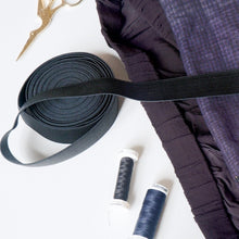 Load image into Gallery viewer, Black ribbon, purple fabric, and spools of thread on a white background