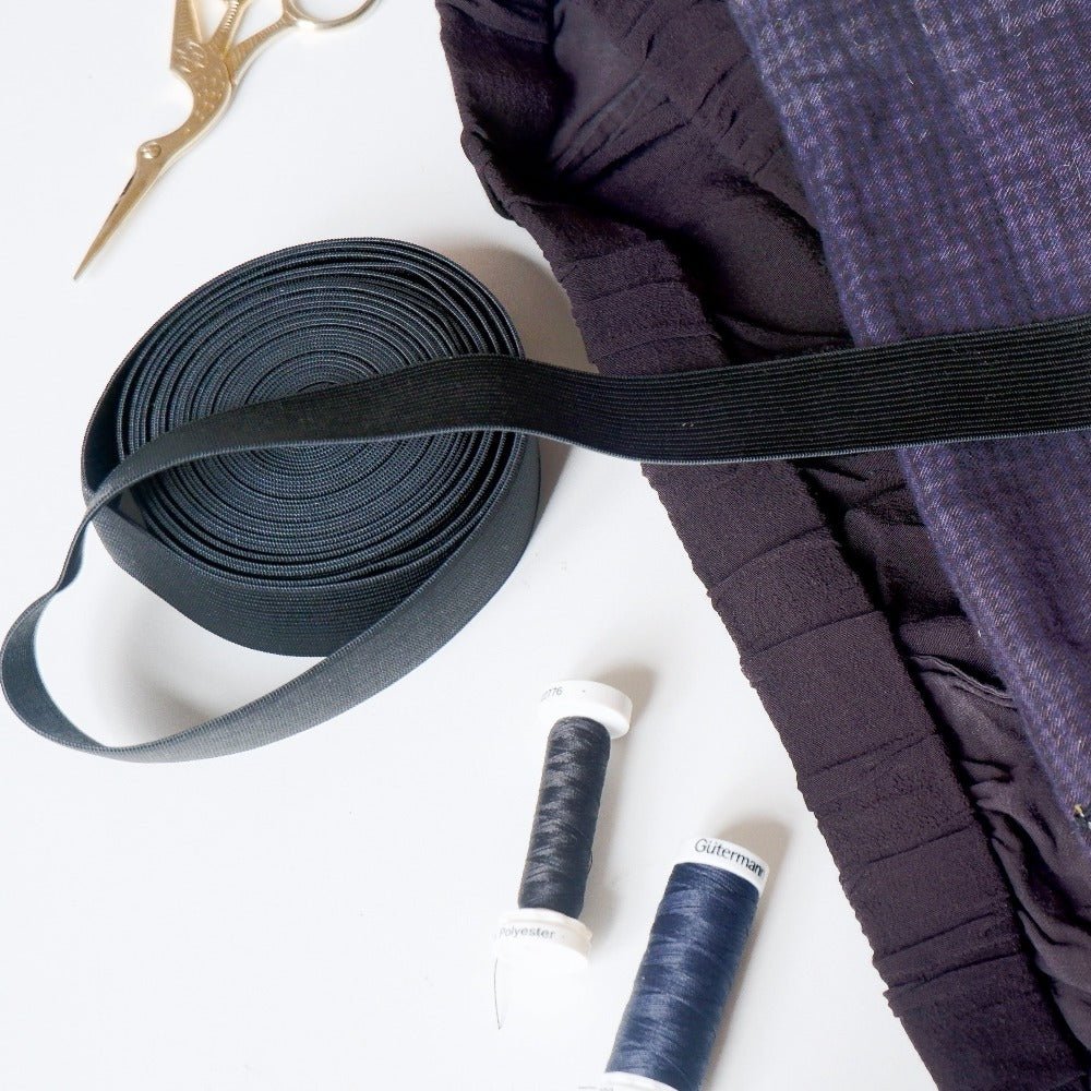 Black ribbon, purple fabric, and spools of thread on a white background