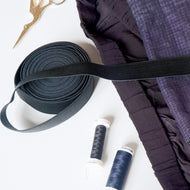 Black ribbon, purple fabric, and spools of thread on a white background