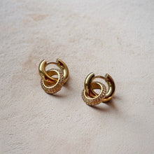 Load image into Gallery viewer, Pair of gold hoop earrings on a beige surface