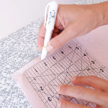 Load image into Gallery viewer, Hand holding a white pen over a transparent ruler with measurements on a textured surface.