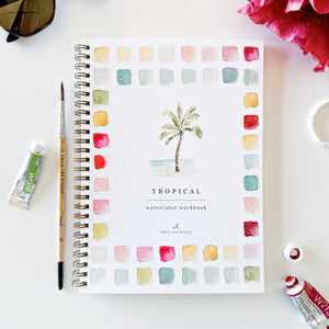 Tropical watercolor workbook with a paintbrush and ink bottle on a white surface