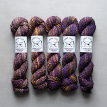 Load image into Gallery viewer, Five skeins of purple and gold yarn with labels on a gray background