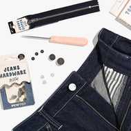Denim hardware kit with buttons, zipper, and tool on a white background