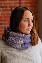 Load image into Gallery viewer, A woman wearing a chunky knit cowl scarf with a purple and gray pattern and leopard print panels, paired with a cream knit sweater against a brick wall background.