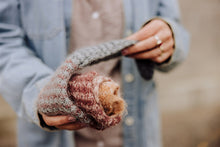 Load image into Gallery viewer, A person wearing a light blue denim jacket holds up a chunky knit glove in a dusty rose and tan colorway, showing the soft fuzzy texture of the knit fabric.
