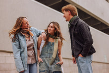 Load image into Gallery viewer, Three young adults standing outdoors against a concrete wall, dressed in casual denim and knit clothing with patterned scarves.