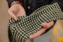 Load image into Gallery viewer, A close-up of a person holding a chunky knit scarf with a black and beige houndstooth pattern.