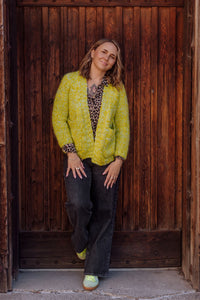 Woman wearing a bright green jacket standing against a wooden wall.