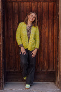 Woman wearing a bright green jacket standing against a wooden wall.