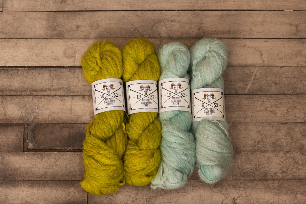 Four skeins of yarn in yellow and green on a wooden surface