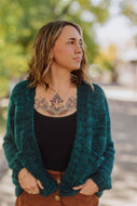 Woman wearing a teal cardigan with a blurred outdoor background