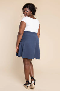 Woman wearing a white top and blue skirt against a beige background