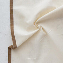 Load image into Gallery viewer, Close-up of beige fabric with brown trim on a light gray background, featuring the brand 'Fableism'.