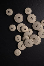 Load image into Gallery viewer, Beige buttons scattered on a dark surface
