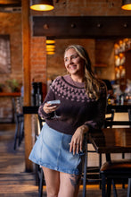 Load image into Gallery viewer, Woman in a cozy bar setting holding a glass, wearing a patterned sweater and denim skirt.