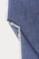 A close-up of a blue woven textile with frayed white edges, folded over against a plain white background.