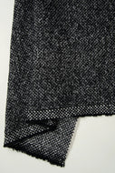 A close-up of a black and white woven fabric, showing a textured herringbone pattern and frayed edges, folded over on a plain white background.