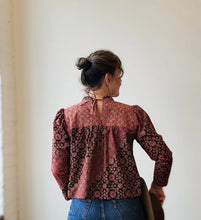 Load image into Gallery viewer, Person wearing a patterned blouse with long sleeves and blue jeans, standing against a plain wall.