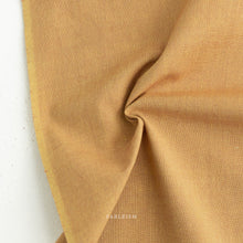 Load image into Gallery viewer, Close-up of beige fabric with 'Fableism' branding on a white background