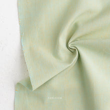 Load image into Gallery viewer, Close-up of light green fabric with 'Fableism' branding on a white background